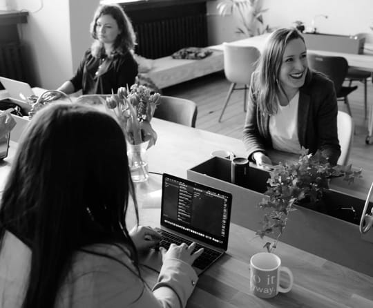 Smiling women, one of them is programming on a laptop